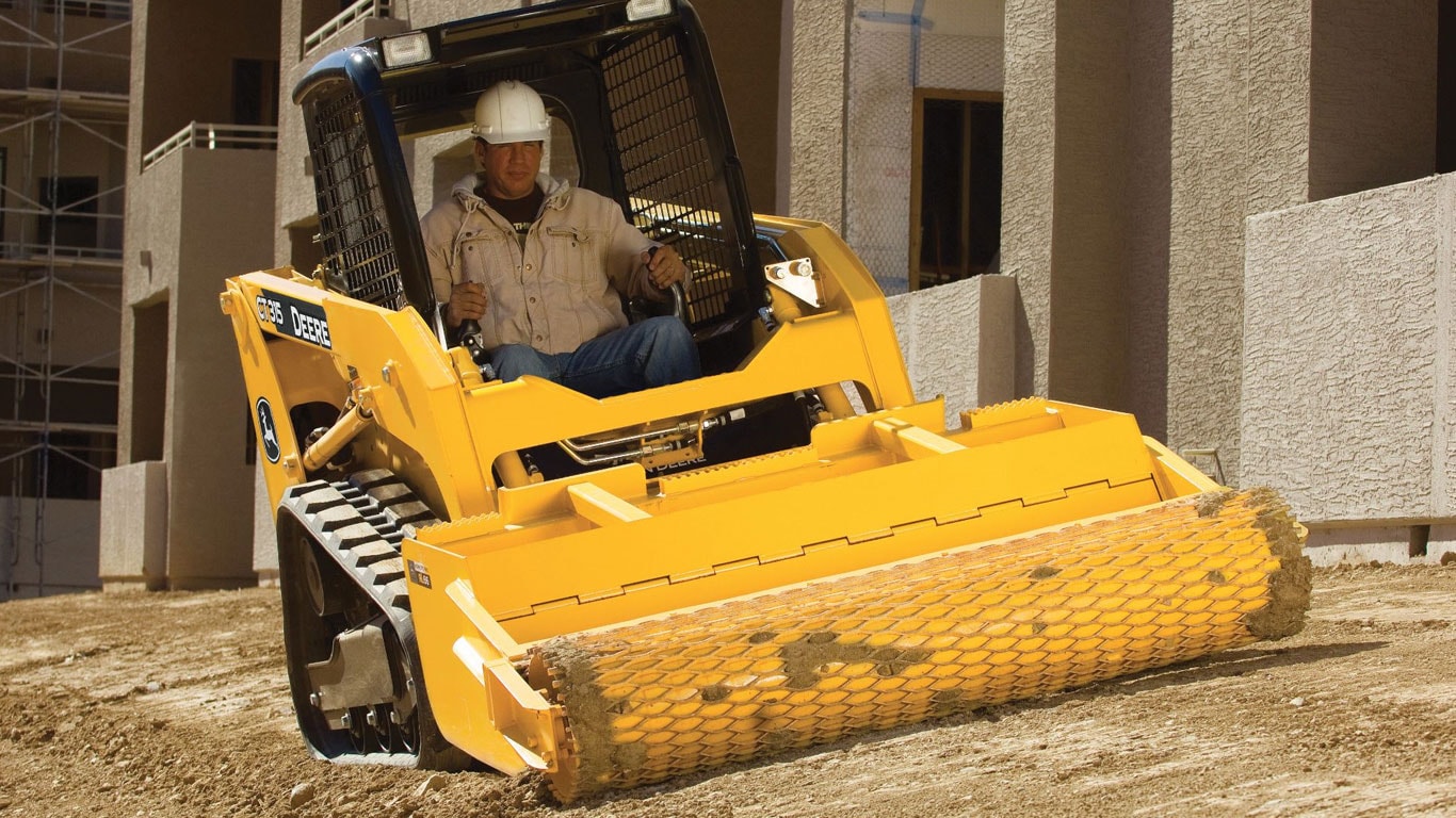 John Deere Skid Steer with Roller Level Attachment compacting dirt on jobsite.